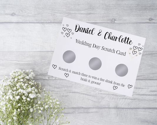  A close-up view of a beautifully designed scratch card with elegant typography and decorative elements. The scratch card features customised names and a wedding date, surrounded by symbols representing hidden prizes. The card is held by a hand, ready to be scratched off, adding an element of anticipation and excitement.