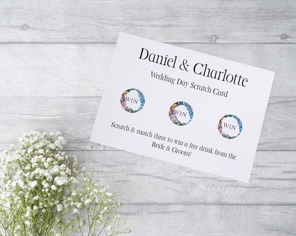  A close-up view of a beautifully designed scratch card with elegant typography and decorative elements. The scratch card features customised names and a wedding date, surrounded by symbols representing hidden prizes.