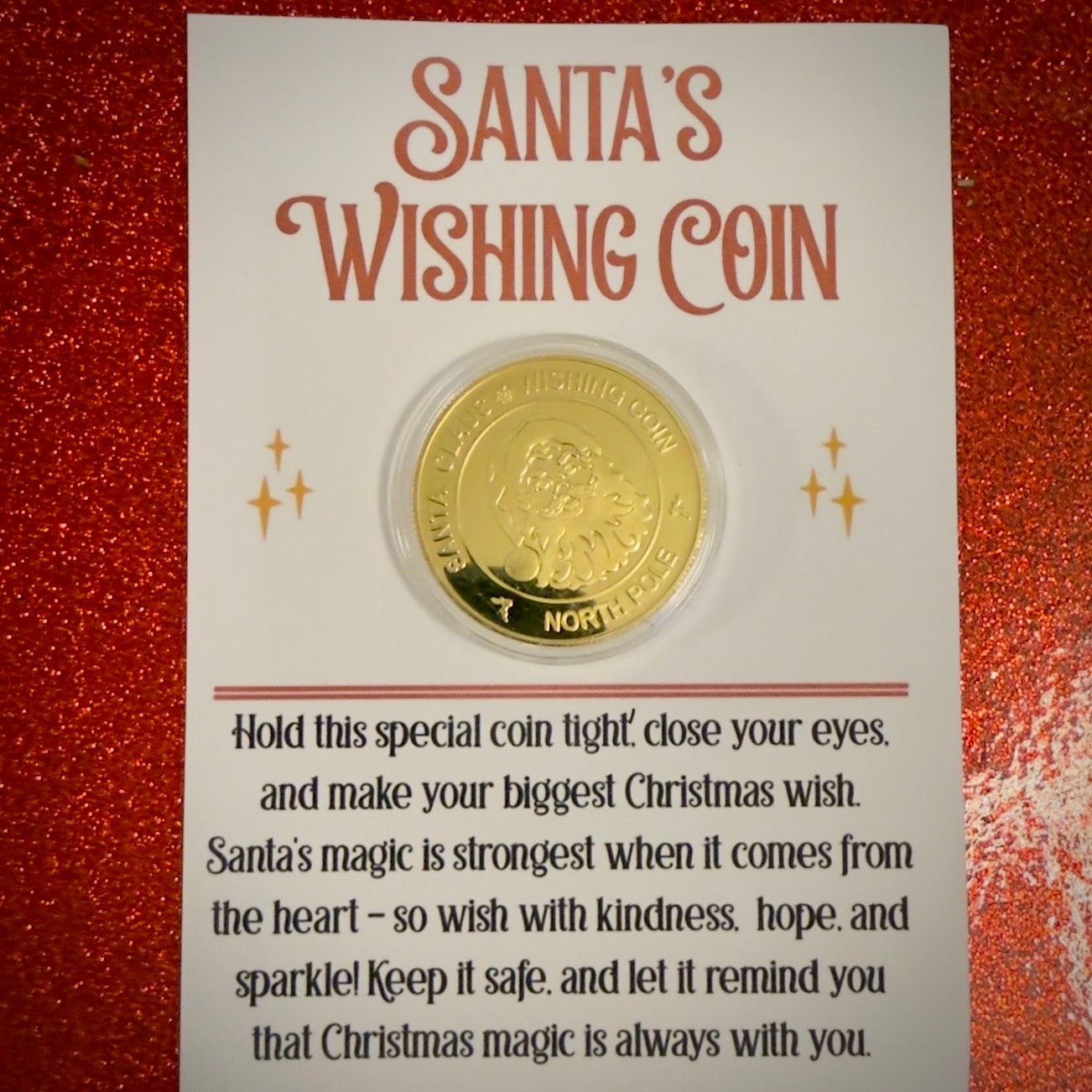 Gold Wishing coin in a clear plastic sleeve on a card with text about Santa's Wishing Coin, against a red glittery background.