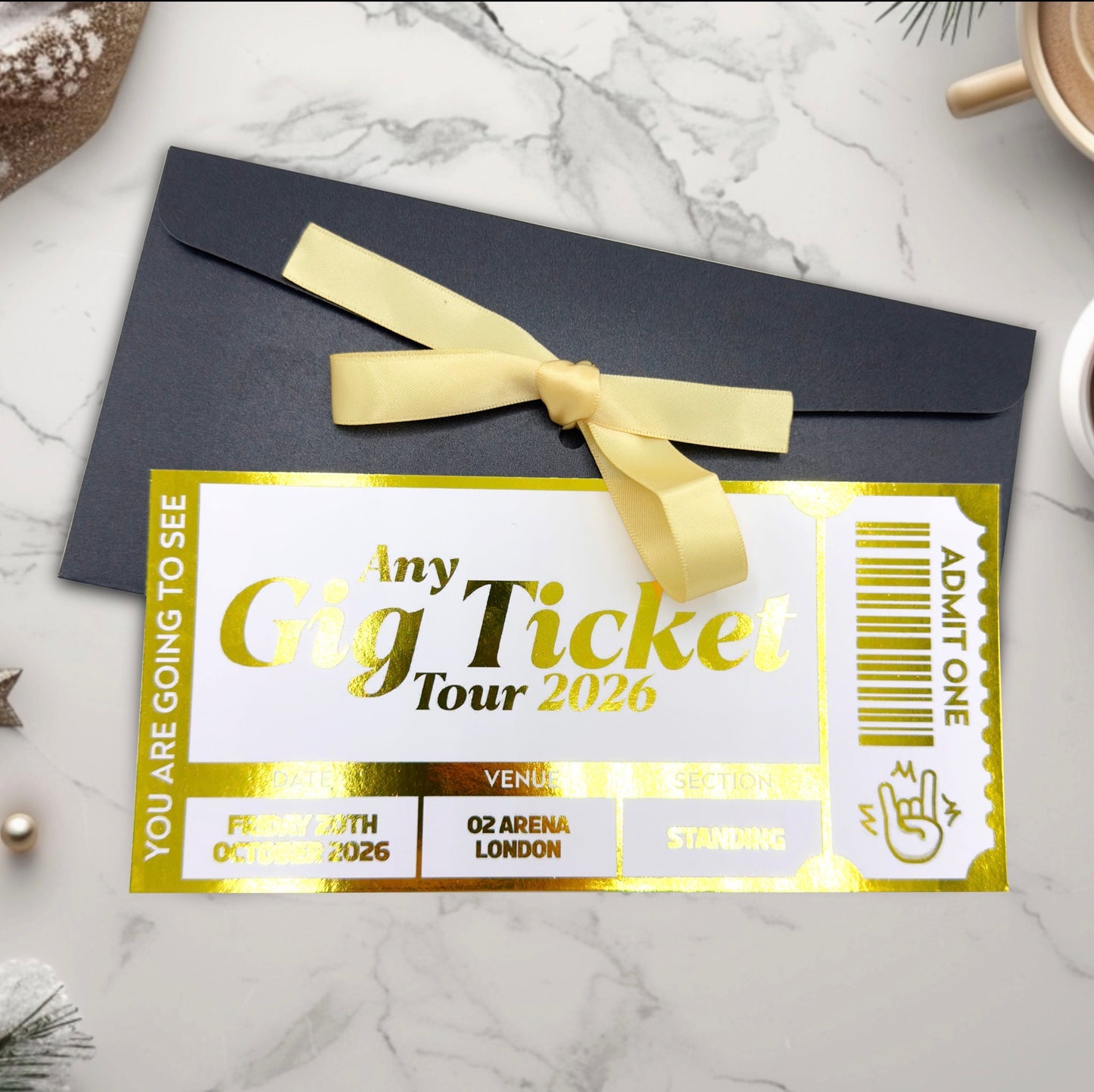 Personalised foil gig ticket with gold text and a yellow ribbon on a dark envelope against a marble background.