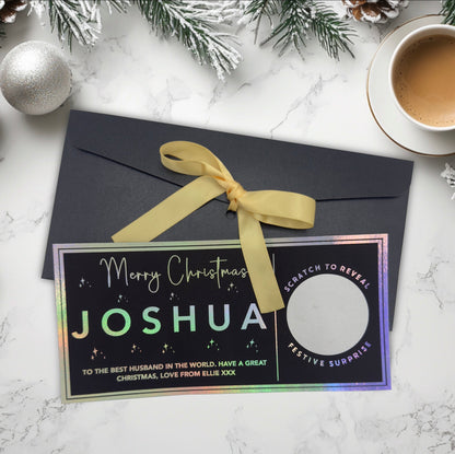 Personalised Christmas scratch-off card with a bow on a marble surface with festive decor.
